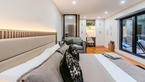 A modern bedroom with a large bed, a seating area, and a view through a sliding glass door.