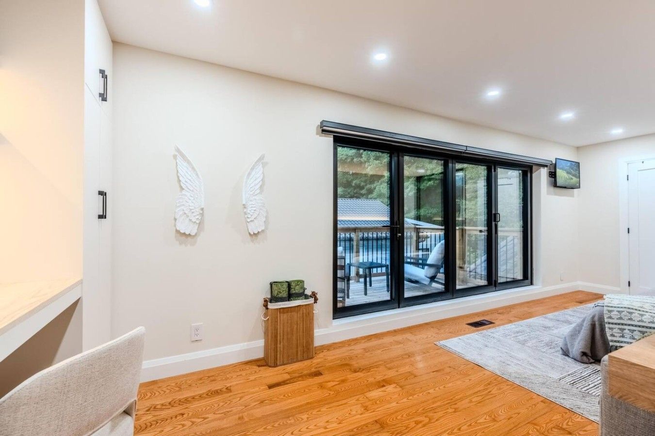 A modern interior with a large sliding glass door leading to an outdoor deck, a wooden floor, and a small side table with a plant.