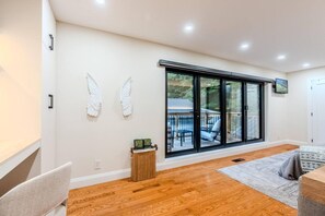 A modern interior with a large sliding glass door leading to an outdoor deck, a wooden floor, and a small side table with a plant.
