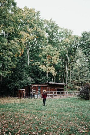 A person walking in a grassy area with trees and a wooden structure in the background.