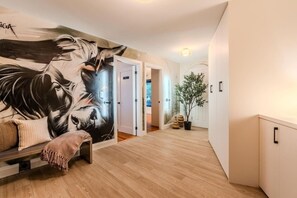 A hallway with a mural, wooden flooring, a bench, and a potted plant.