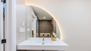 A modern bathroom with a white sink, a mirror, and a shower area.