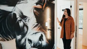 Una habitación con un mural grande en la pared, un sofá con una manta y una persona de pie junto a una puerta.