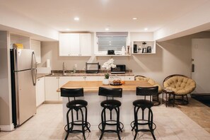 Une cuisine moderne dotée d’un îlot central, de tabourets de bar, d’un réfrigérateur et d’une chaise.