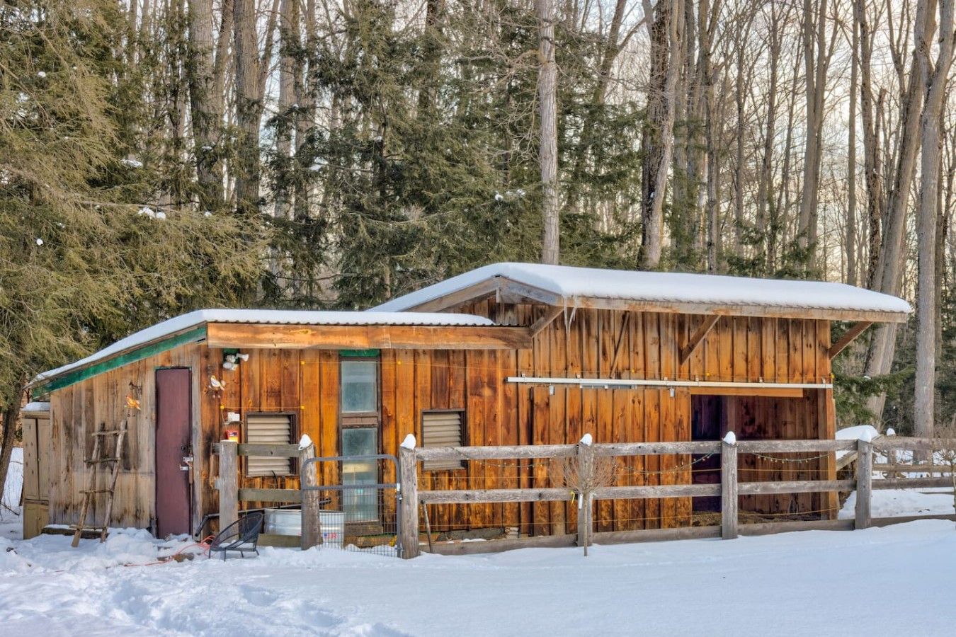 A rustic cabin with a wooden exterior, a fenced yard, and a snow-covered roof.