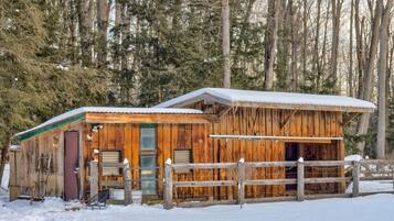 A rustic cabin with a wooden exterior, a fenced yard, and a snow-covered roof.