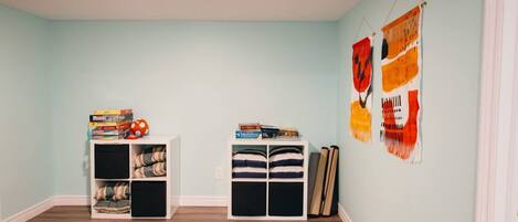 A room with light blue walls, wooden flooring, two white shelving units, and two abstract wall hangings.