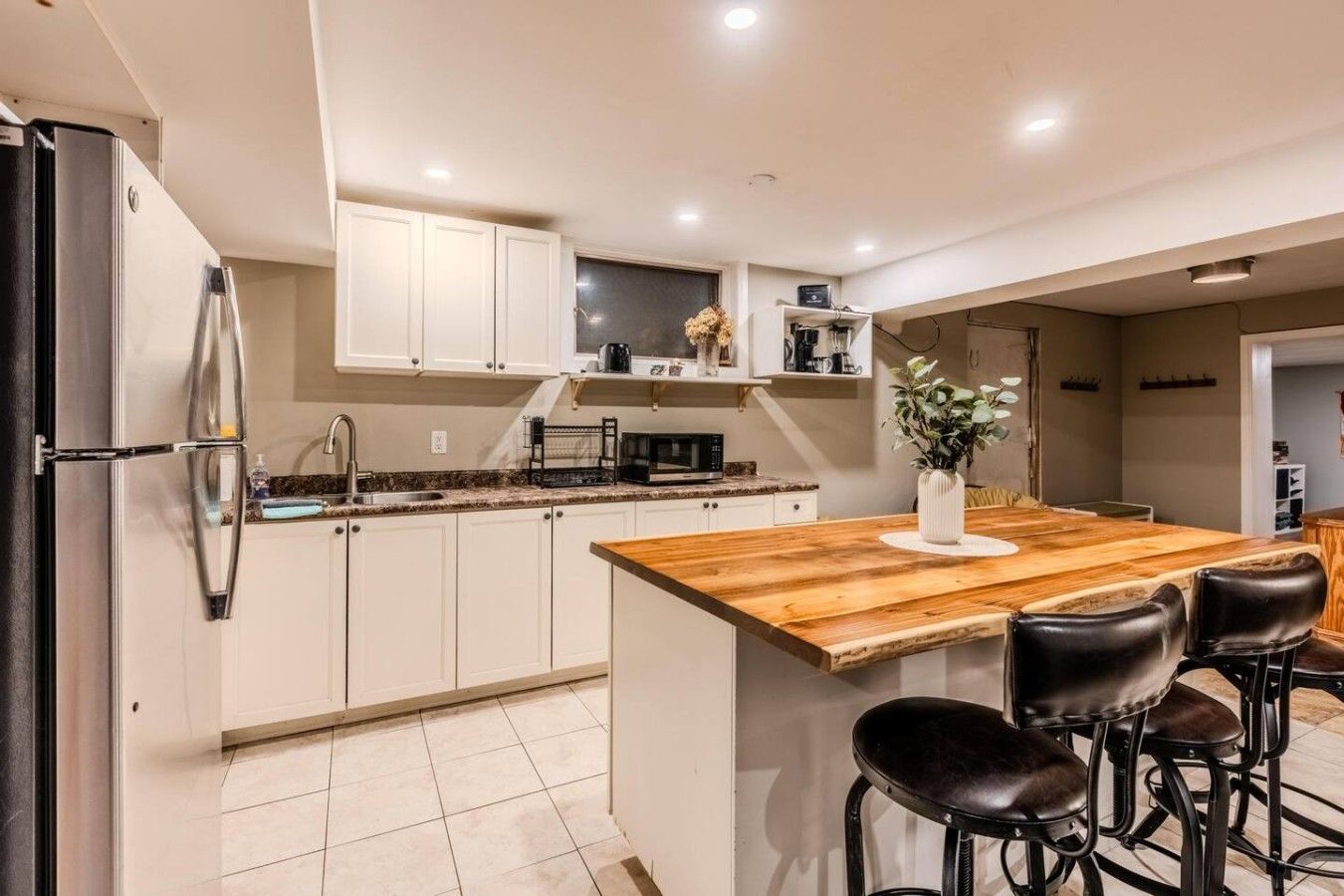 A modern kitchen with white cabinets, a stainless steel refrigerator, a wooden island with bar stools, and a microwave.
