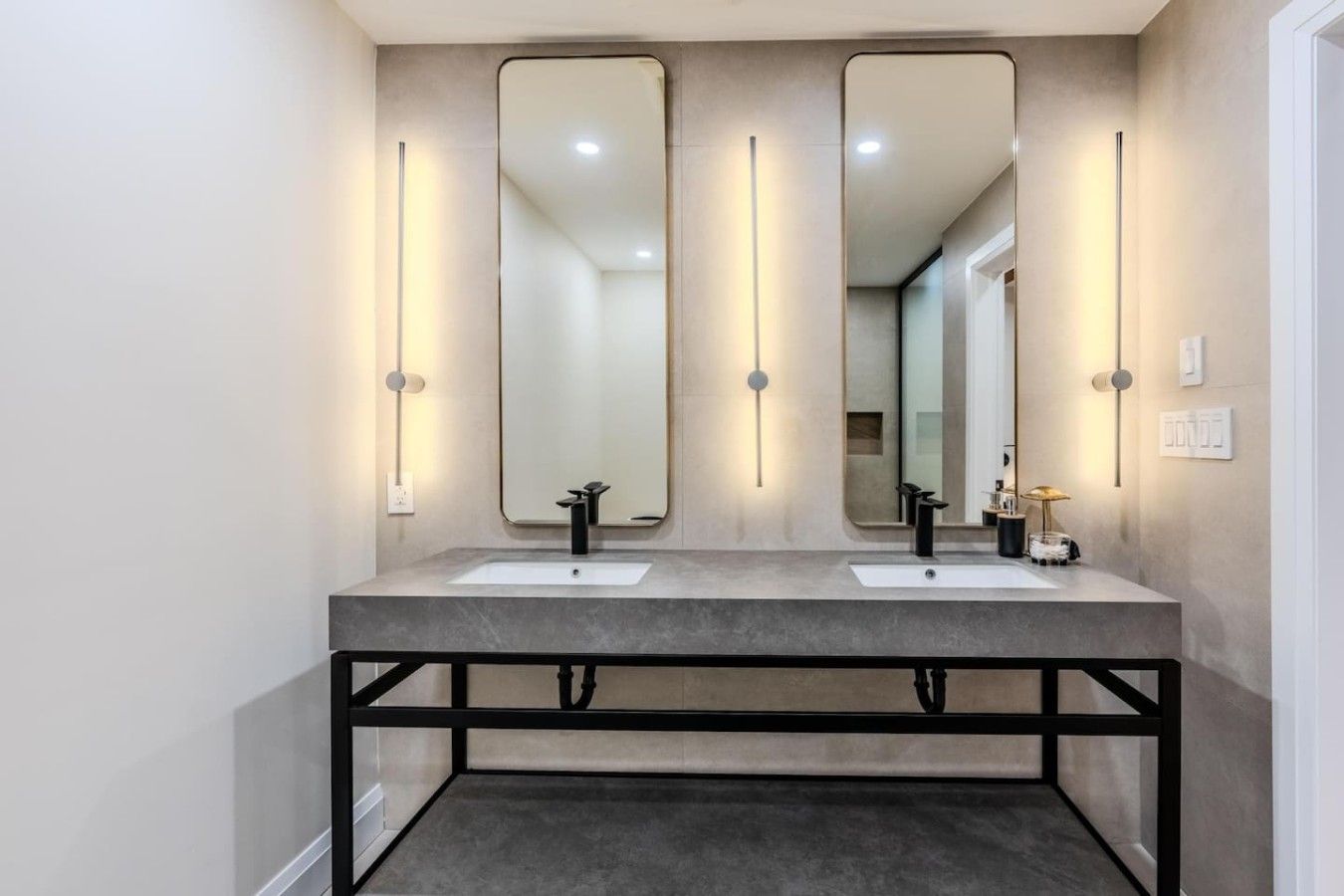 A modern bathroom with two sinks, large mirrors, and wall-mounted lighting.