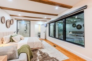 A bedroom with a large window, a bed, a bedside table, and a shower area.