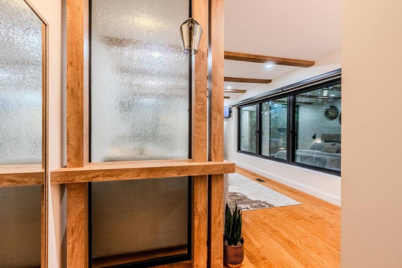 A modern interior with wooden flooring, frosted glass partitions, and a potted plant.