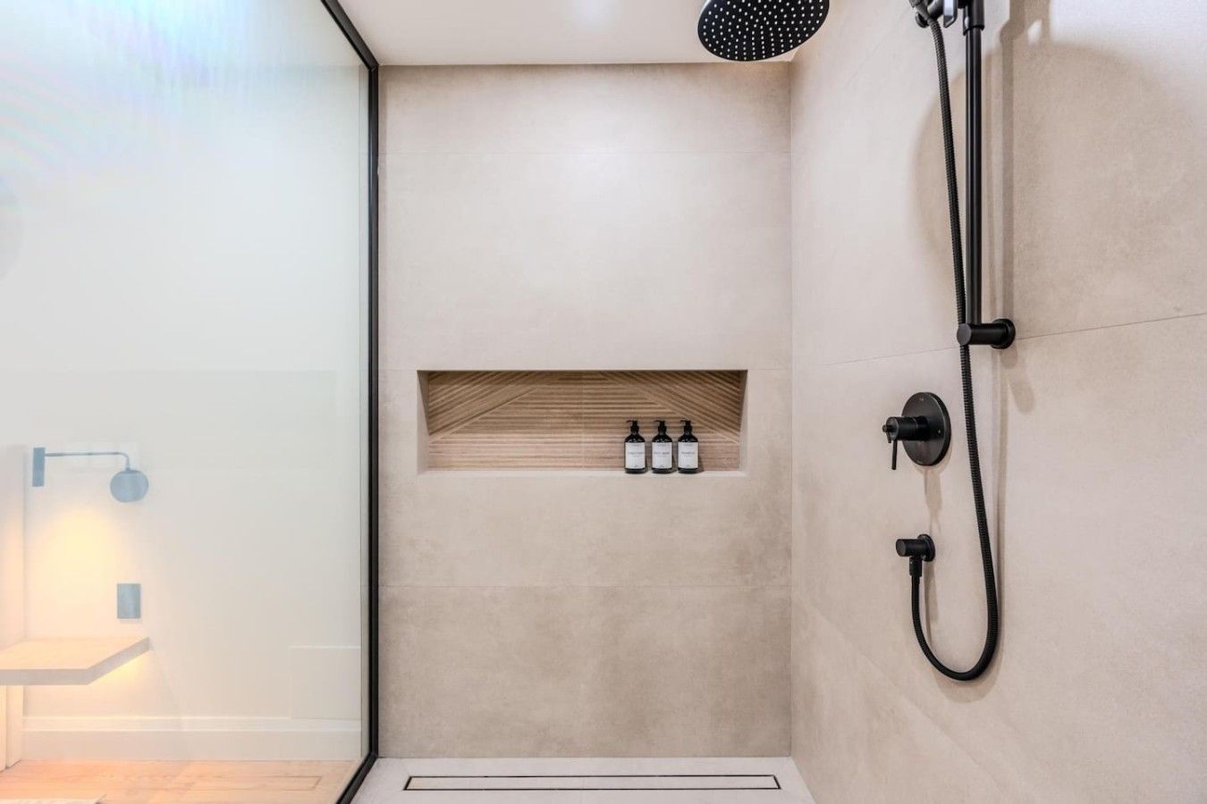 A modern shower area with a built-in shelf for toiletries, a handheld showerhead, and a wall-mounted faucet.