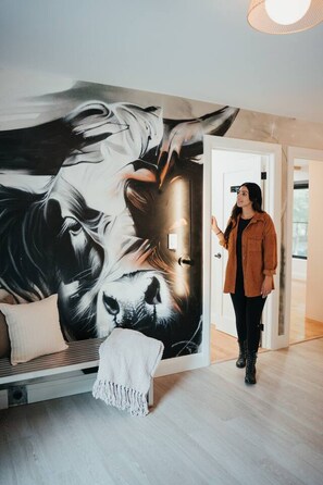 A room with a large wall mural, a sofa with a throw blanket, and a person standing by a door.