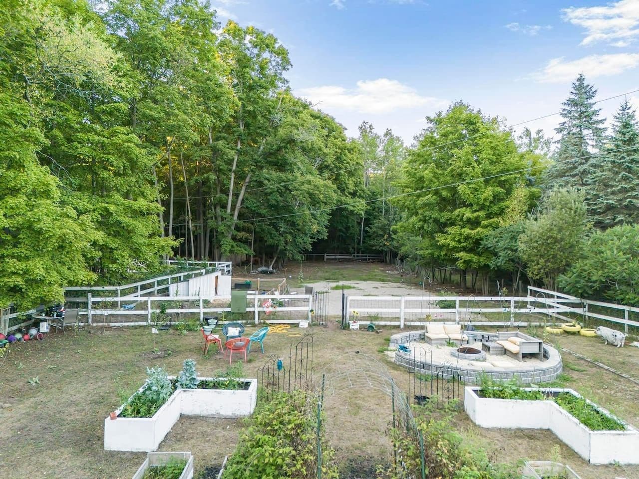 A fenced outdoor area with a circular seating arrangement, surrounded by trees and a grassy field.