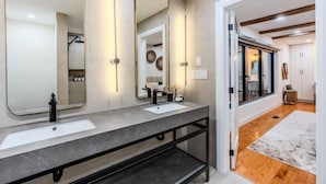 A modern bathroom with two sinks, a large mirror, and a walk-in shower.