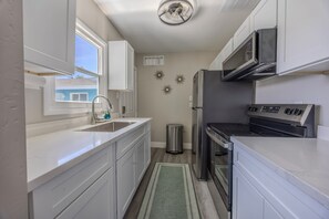 A compact kitchen with white cabinetry, a stainless steel refrigerator, a stove, and a microwave. - Cozy 1-bedroom Suite in the Art District Downtown Las Vegas (Las Vegas)