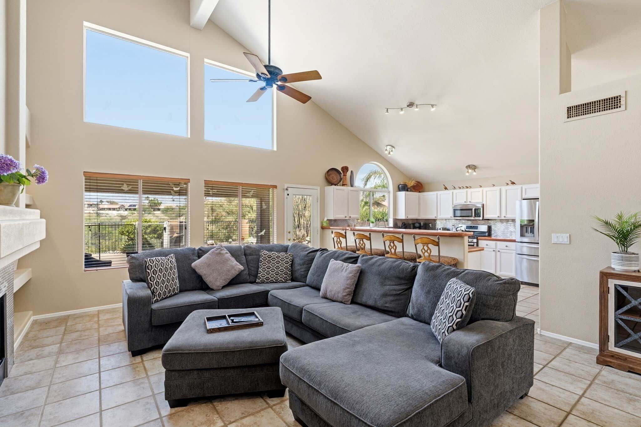 A spacious living room with a sectional sofa, a dining area, and a kitchen with white cabinets.