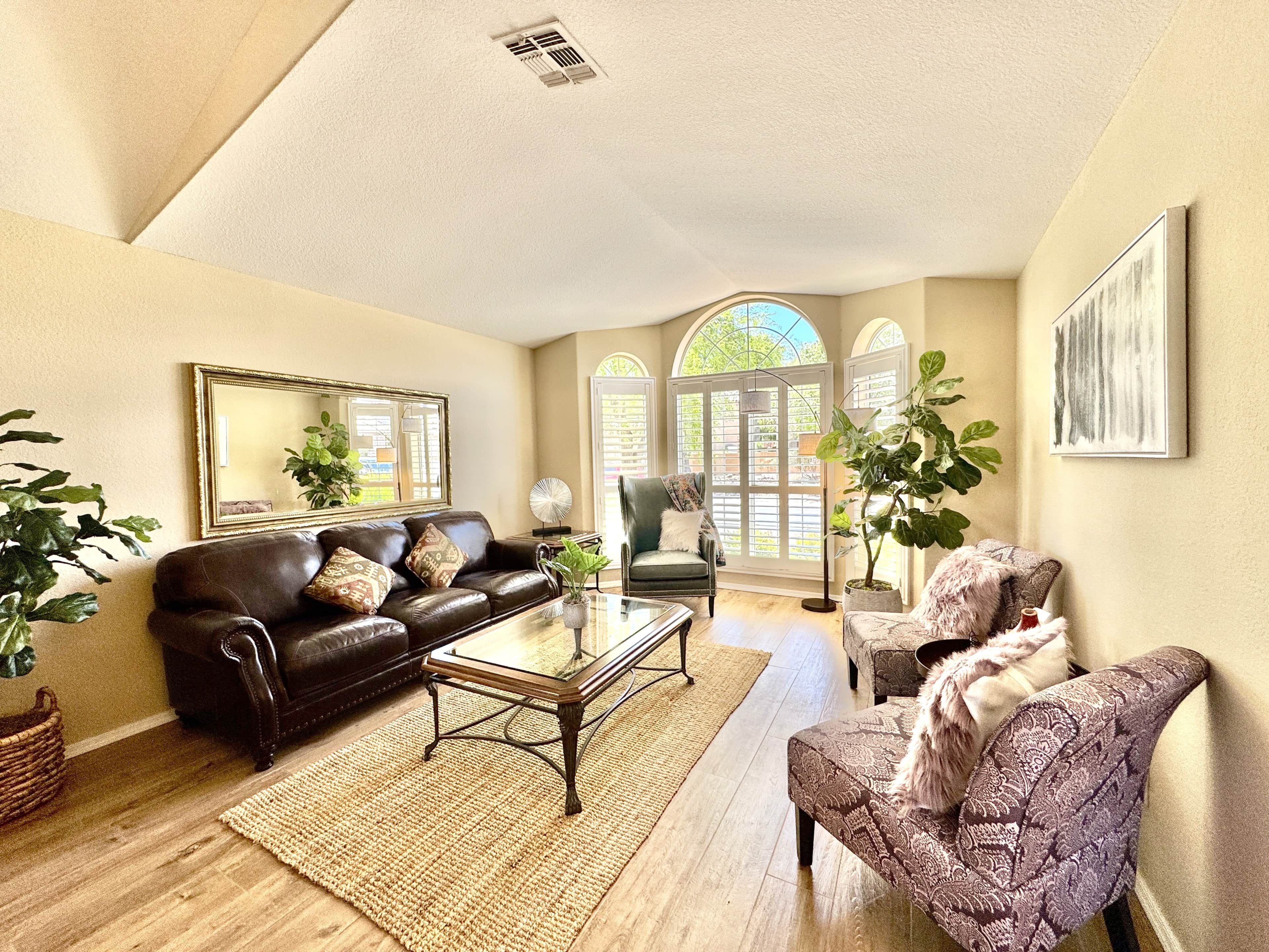 A spacious living room with a leather sofa, a patterned armchair, a glass coffee table, and a large mirror on the wall.