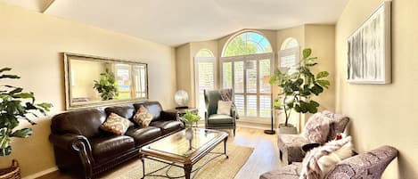 A spacious living room with a leather sofa, a patterned armchair, a glass coffee table, and a large mirror on the wall.