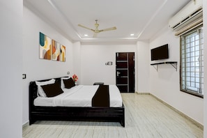 A hotel room with a bed, ceiling fan, artwork, TV, and a window.