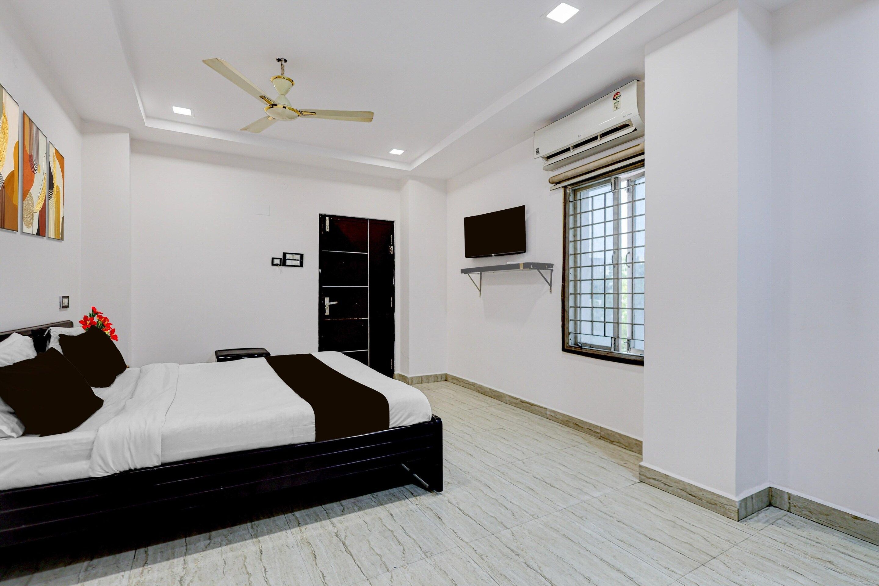 A bedroom with a bed, a ceiling fan, an air conditioning unit, a TV, and a window.