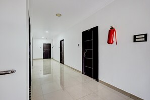 Un pasillo con un extintor sujeto a la pared, una puerta con marco negro y suelo de baldosas.