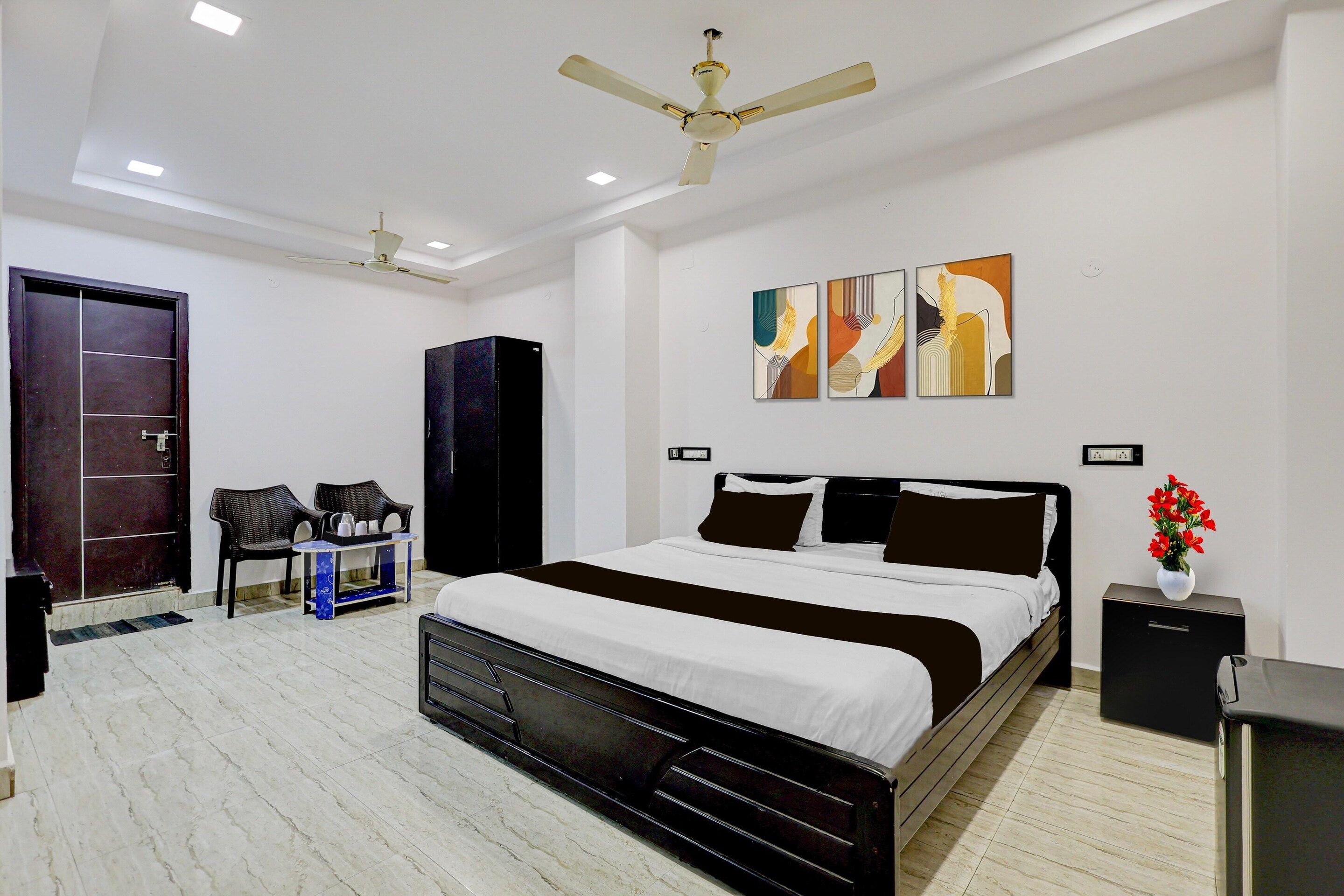 A bedroom with a bed, a wardrobe, a desk, chairs, and artwork on the wall.