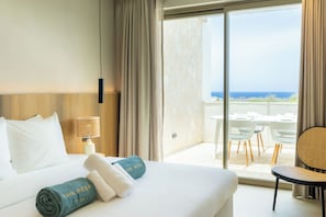 A hotel room with a bed, a nightstand, a lamp, a view of the ocean through a large window, and a balcony with outdoor furniture. - The Reef Superior at Blue Bay (Blue Bay)