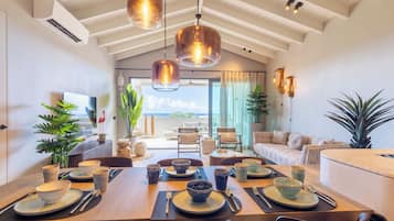 A dining area with a high ceiling, pendant lighting, and a view of the outdoors.