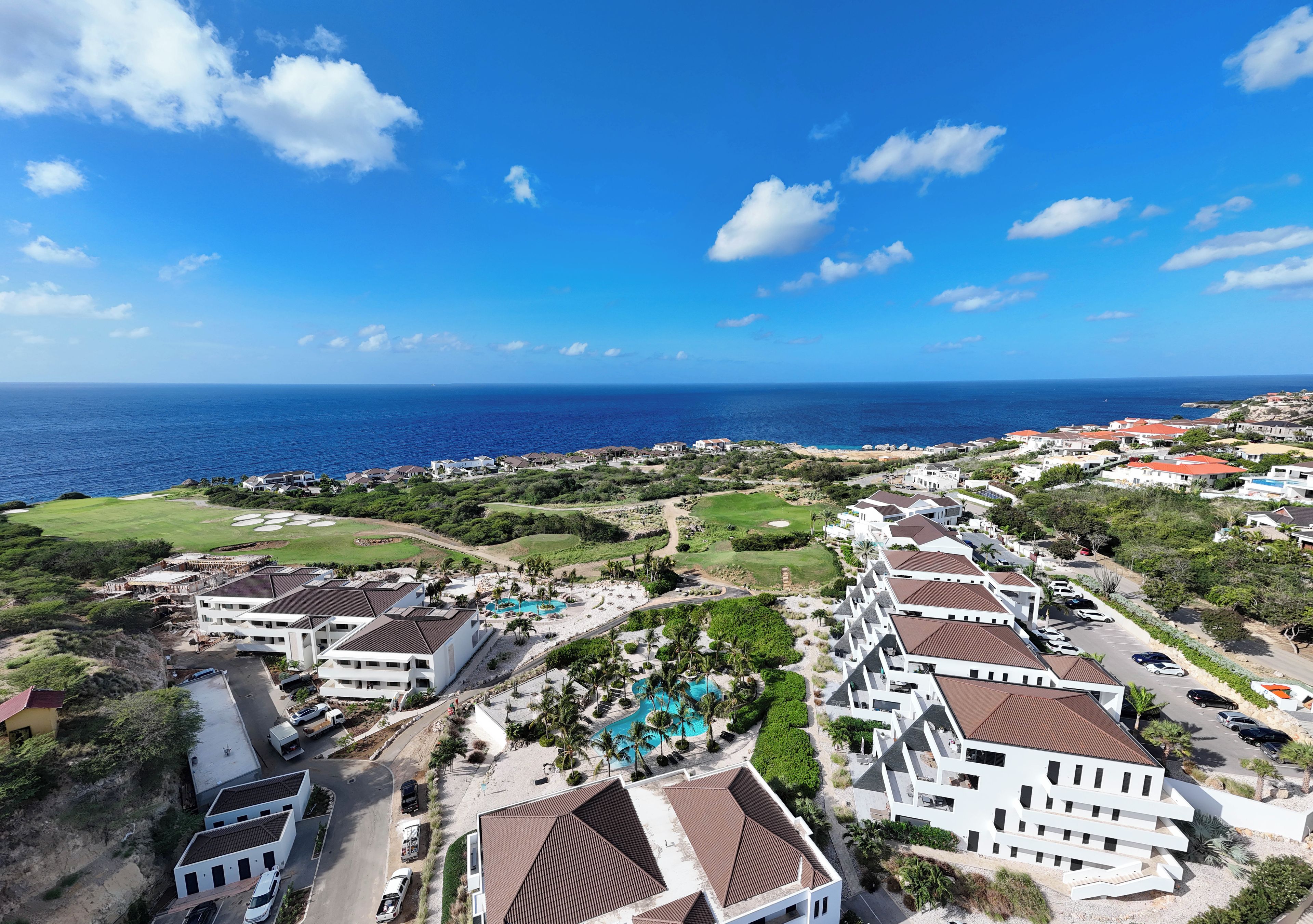 A coastal resort with multiple buildings, a swimming pool, and a view of the ocean.