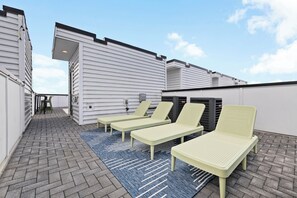 Eine Dachterrasse mit drei Liegestühlen und einem blauen Teppich mit Muster.