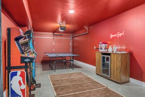 Ein Zimmer mit Tischtennisplatte, Basketball-Arcade-Spiel und einer Neonreklame.