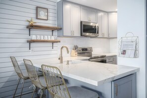 A modern kitchen with white cabinetry, a marble countertop, and a built-in oven. - Kaanapali, Kulakane, Spacious 4 BR, Beachfront, Sleeps 14 (Lahaina)
