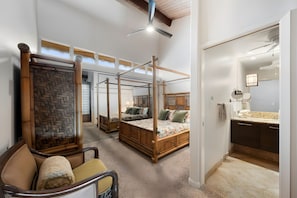 A spacious bedroom with a four-poster bed, a sitting area with a chair, and a bathroom with a vanity and mirror. - Kaanapali, Kulakane, Spacious 4 BR, Beachfront, Sleeps 14 (Lahaina)