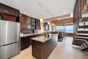 A modern kitchen with a central island, dark wood cabinets, and a stainless steel refrigerator. - Kaanapali, Kulakane, Spacious 4 BR, Beachfront, Sleeps 14 (Lahaina)