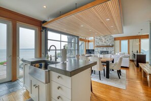 Een moderne keuken met een groot eiland, een eethoek met een houten tafel en uitzicht op de zee door grote ramen.