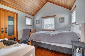 Een slaapkamer met een schuine kap, een bed, een bureau met een computer en een stoel.