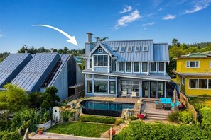 Een moderne, tweelaagse woning met een grote glazen voorgevel, een zwembad en een verzorgde tuin.