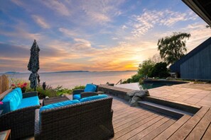 Een houten terras met rieten meubilair en uitzicht op zee bij zonsondergang.