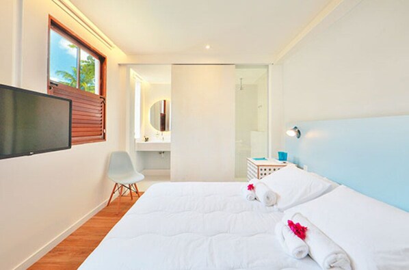 A hotel room with a bed, a TV, a chair, a bathroom, and a view of the outdoors.