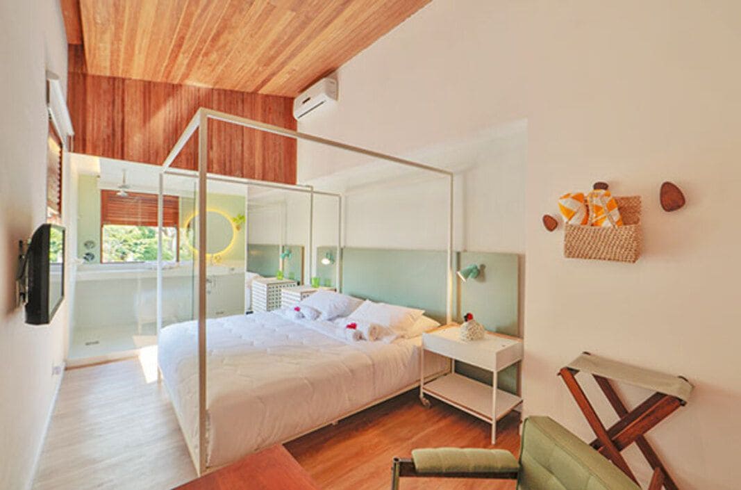 Un dormitorio moderno con cama con dosel, mesita de noche, una silla y ventana con vistas a la vegetación.