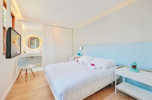 A modern hotel room with a large bed, a desk, a chair, and a bedside table.