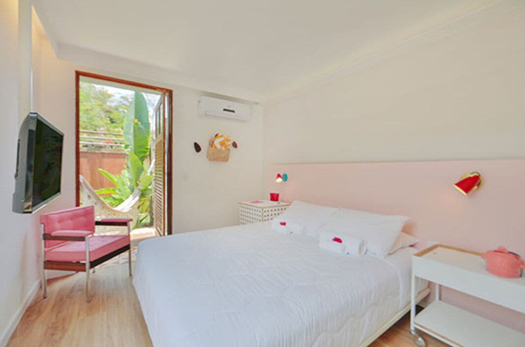 Un dormitorio con cama, una silla, televisor, mesita de noche y ventana con vista a la vegetación.