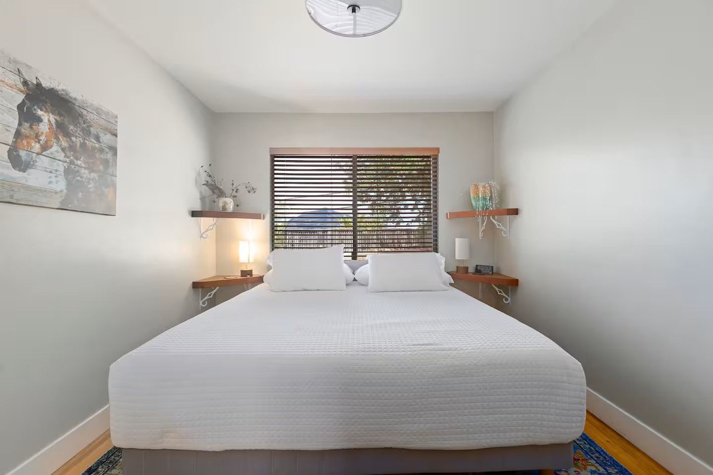 Une chambre avec un grand lit, deux tables de chevet avec des lampes, une fenêtre avec des stores et une étagère murale décorative.