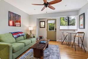 Un salon avec un canapé vert, une table basse en bois, un ventilateur de plafond et un coin repas comprenant une table et des chaises.