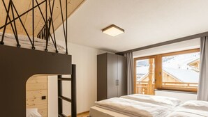 Un dormitorio con literas, una cama individual, un armario y una ventana con vistas a un paisaje nevado.