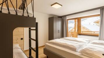 A bedroom with a bunk bed, a single bed, a wardrobe, and a window with a view of a snowy landscape.