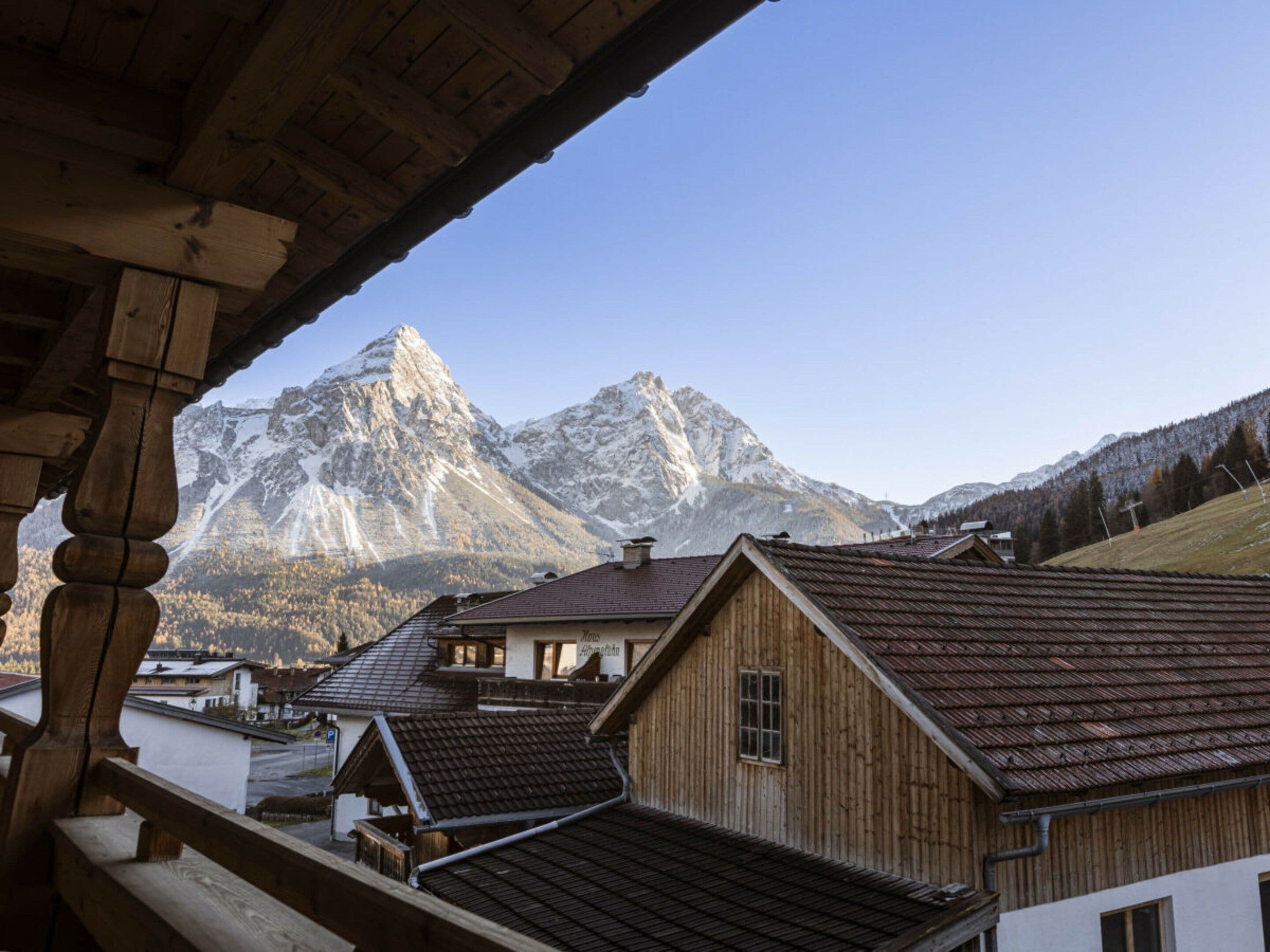 A wooden building with a sloped roof, a visible window, and a mountain backdrop.