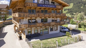 Un edificio de varios pisos con balcones, con la leyenda 'ALPS RESORTS', rodeado de un paisaje montañoso.