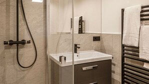 Un baño moderno con cabina de ducha de vidrio, un lavamanos blanco y un perchero para toallas.